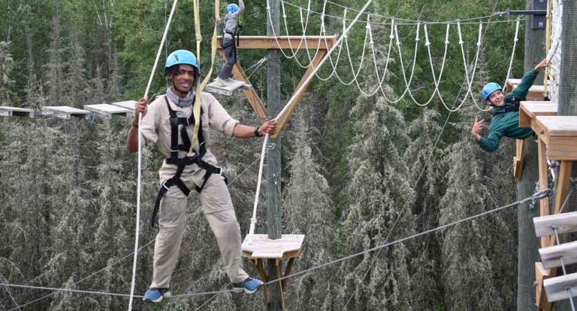 two students smile as they are suspended on a ropes course with outward bound course